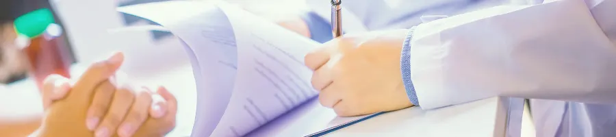 A doctor writing on paper while another person is across the table